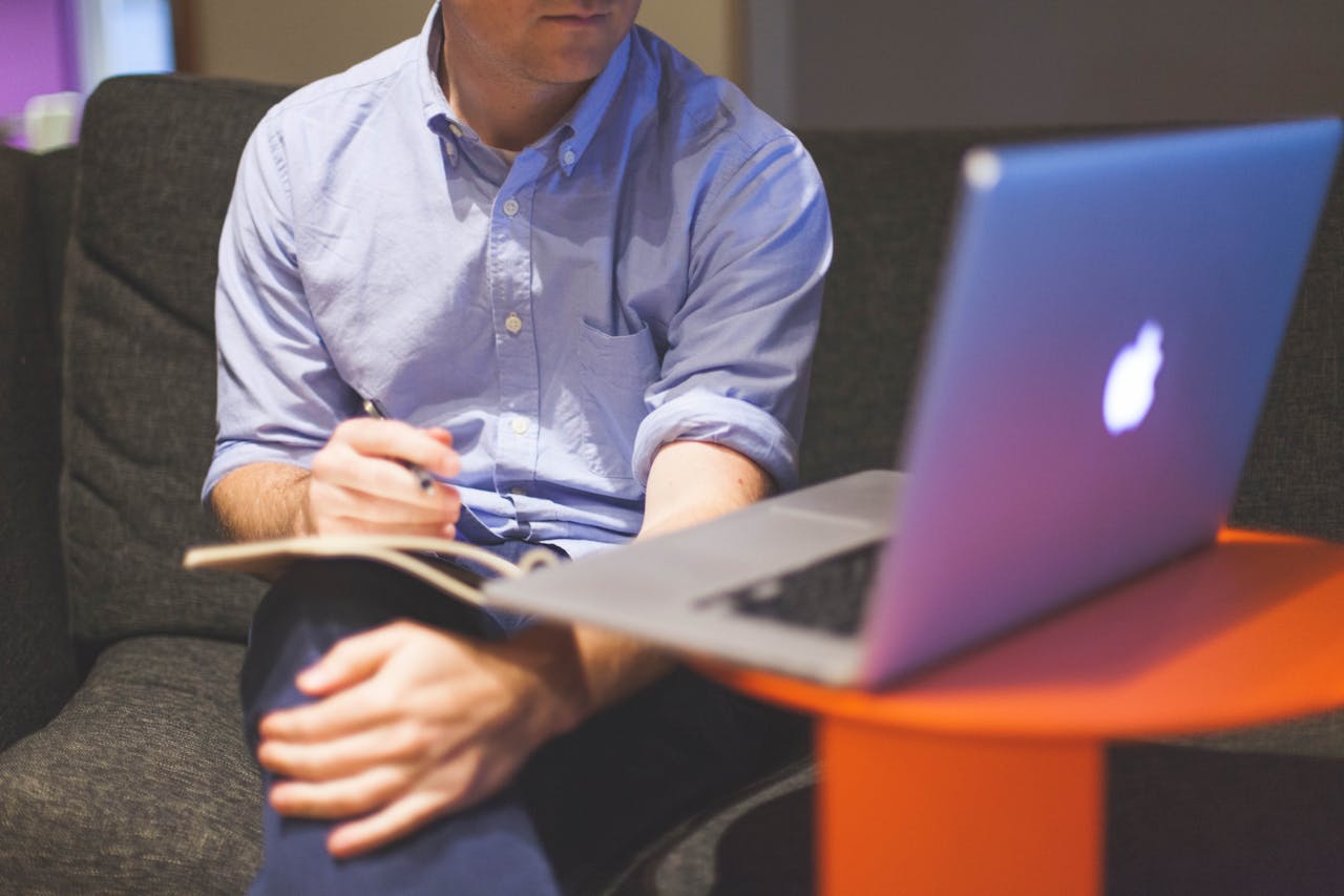 Man working remotely with laptop and notebook, noting ideas.