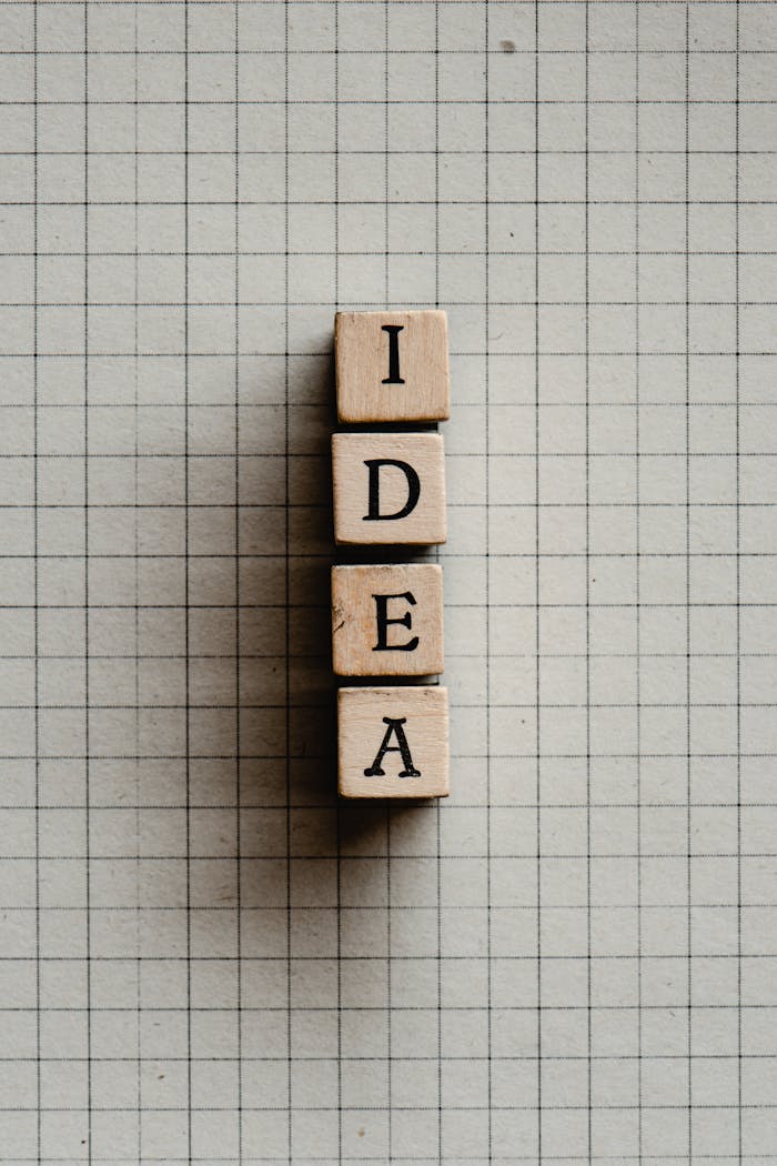 Vertical shot of wooden letter tiles spelling 'IDEA' on grid paper, creative concept.